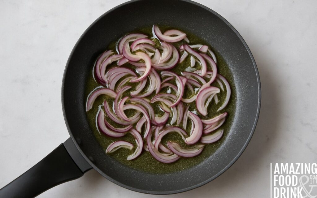 Sliced red onions saut&eacute;ing in sunflower oil in a black non-stick frying pan on marble surface, illustrating early caramelisation step for healthy burrito bowl recipe