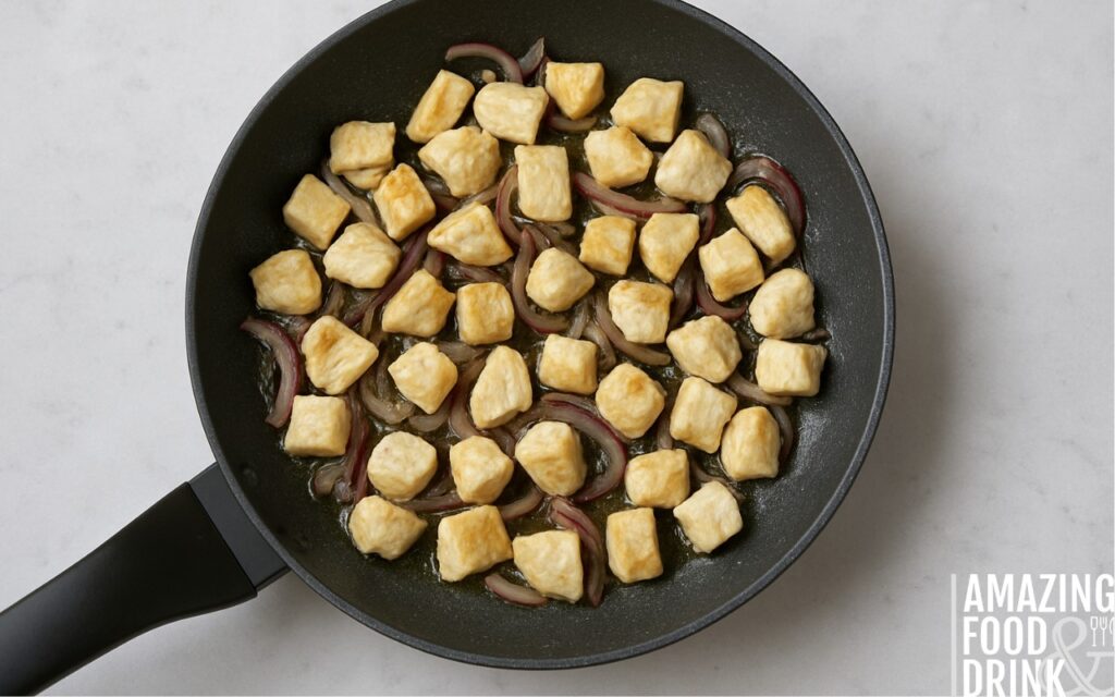 Diced chicken breast cooking with softened red onions in sunflower oil in a non-stick frying pan, illustrating even browning technique for healthy burrito bowl recipe