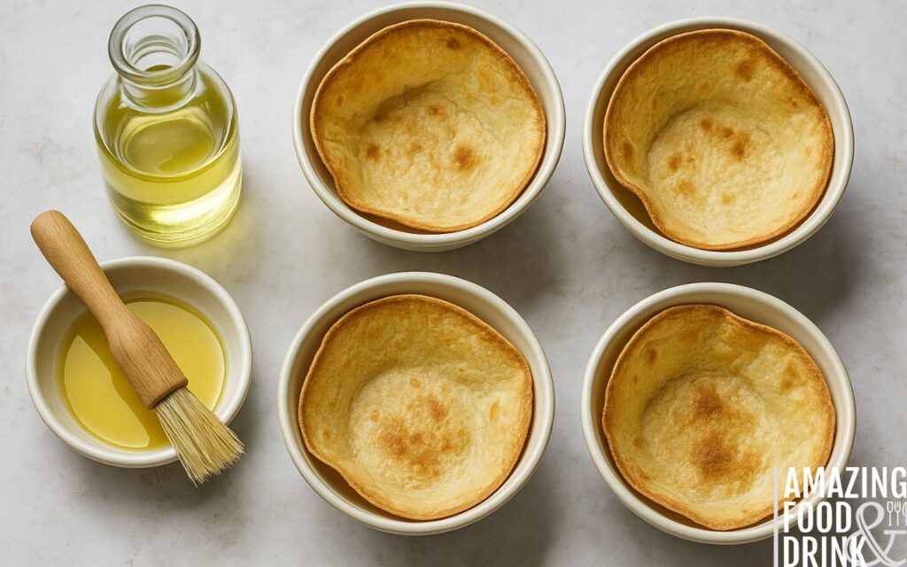 Golden baked tortilla bowls in ovenproof dishes with sunflower oil and pastry brush on marble countertop, illustrating step-by-step method for healthy burrito bowl preparation