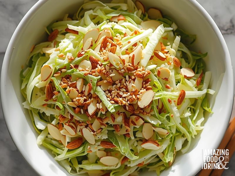 Asian-style cabbage slaw with almonds and toasted sesame seeds in white serving bowl