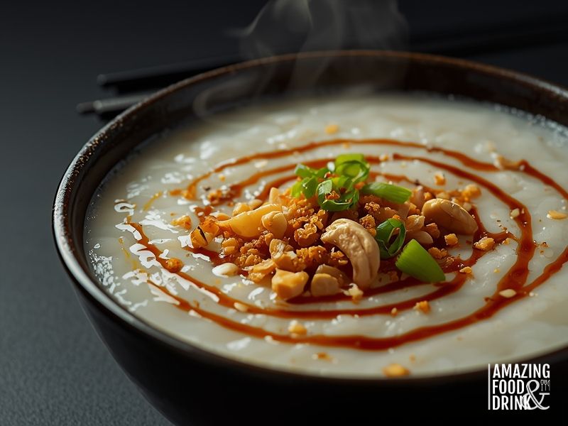 Steaming bowl of savoury congee topped with fried shallots, spring onions, peanuts, and sesame oil in dark ceramic bowl
