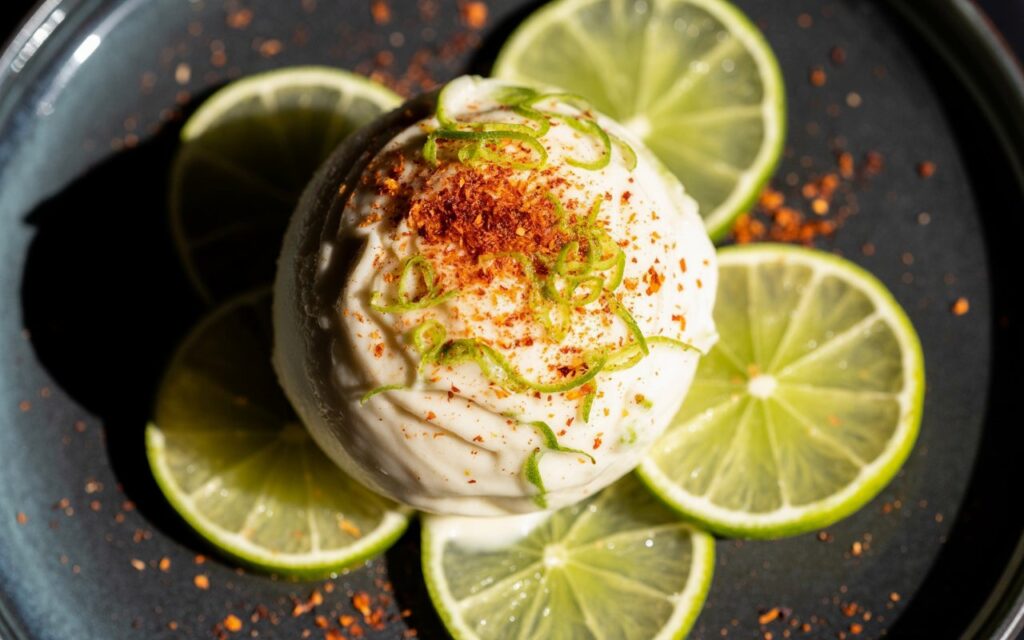 Latin American: Coconut lime ice cream with chilli flakes and lime zest, bold colour contrast, modern plating.
