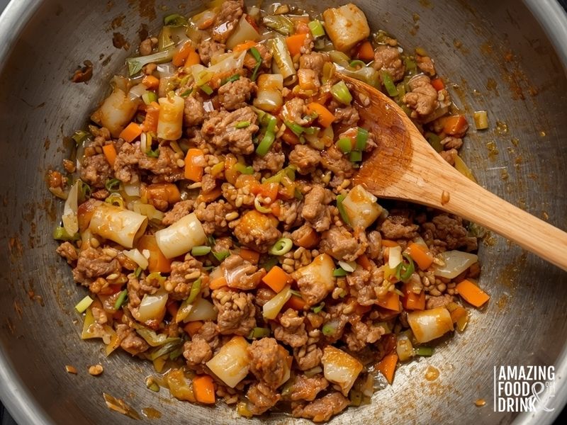 Cooked pork and vegetable egg roll filling in wok with visible seasoning
