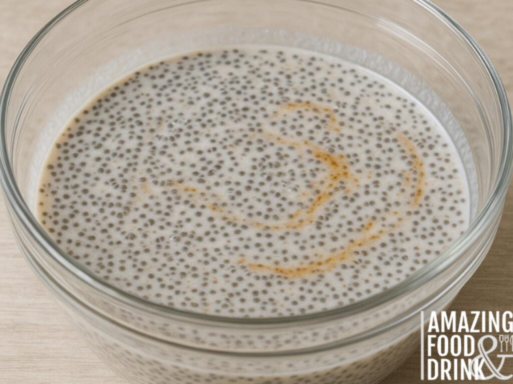 "Glass mixing bowl filled with chia seeds soaking in creamy coconut milk and swirls of vanilla extract, placed on a light wooden surface."








