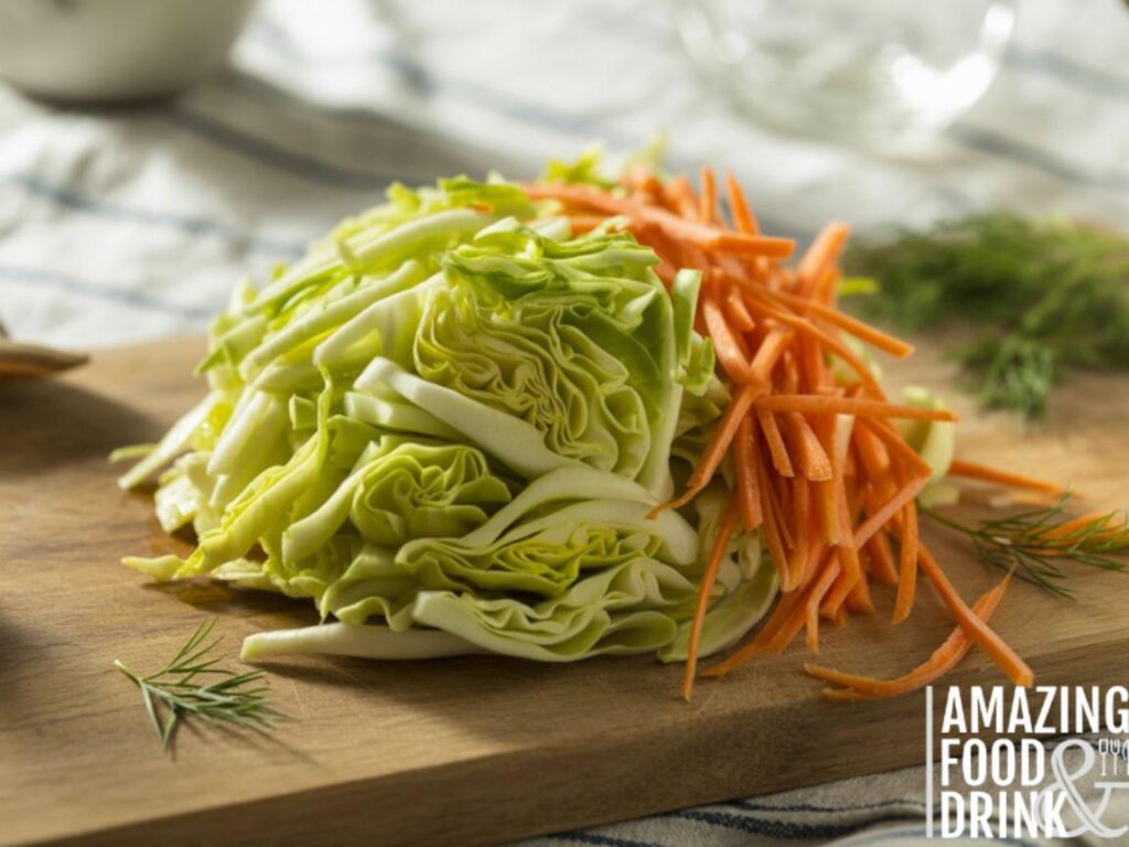 A photograph of a close-up view showcasing a mound of finely shredded cabbage and julienned carrots meticulously arranged on a rustic wooden cutting board. The cabbage has a vibrant green hue with tightly packed leaves, while the carrots display a bright orange color with thin, uniform strands, all glistening with a light coating of olive oil. Scattered around the vegetables are a few sprigs of fresh dill and parsley, adding subtle pops of green. Soft, diffused sunlight illuminates the scene, casting gentle shadows and highlighting the textures of the fresh ingredients.