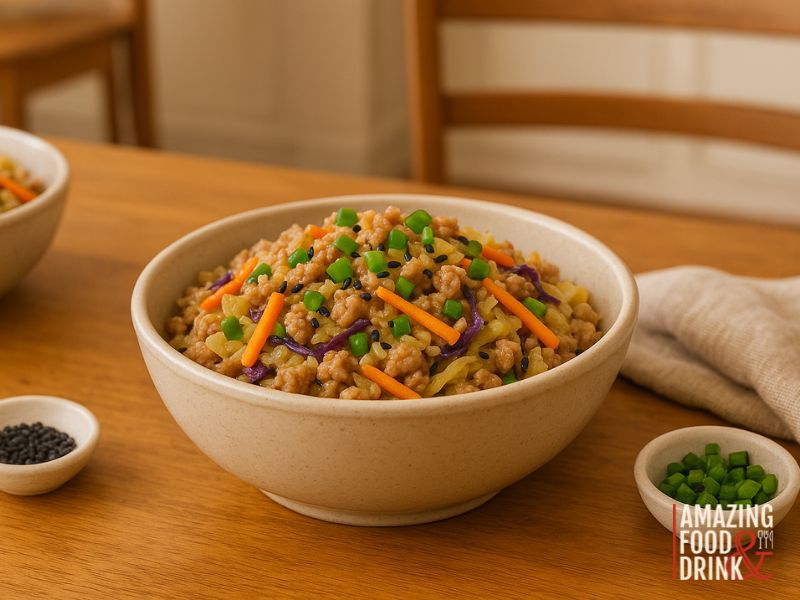 A bowl of mixed grain Unstuffed Egg Roll stir-fry with carrots, cabbage, green onions, and black sesame seeds on a wooden table, with a napkin and small bowl of green onions nearby&mdash;a Chinese-American classic made easy.