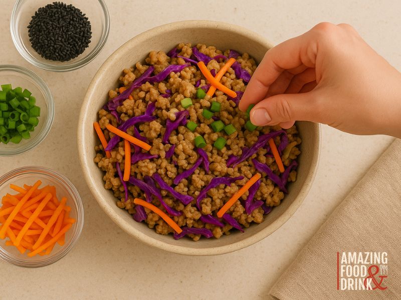 A hand sprinkles chopped green onions on a bowl of egg roll in a bowl&mdash;a Chinese-American dish featuring stir-fried rice with ground meat, shredded carrots, and purple cabbage. Small bowls of black sesame seeds, carrots, and onions are nearby.